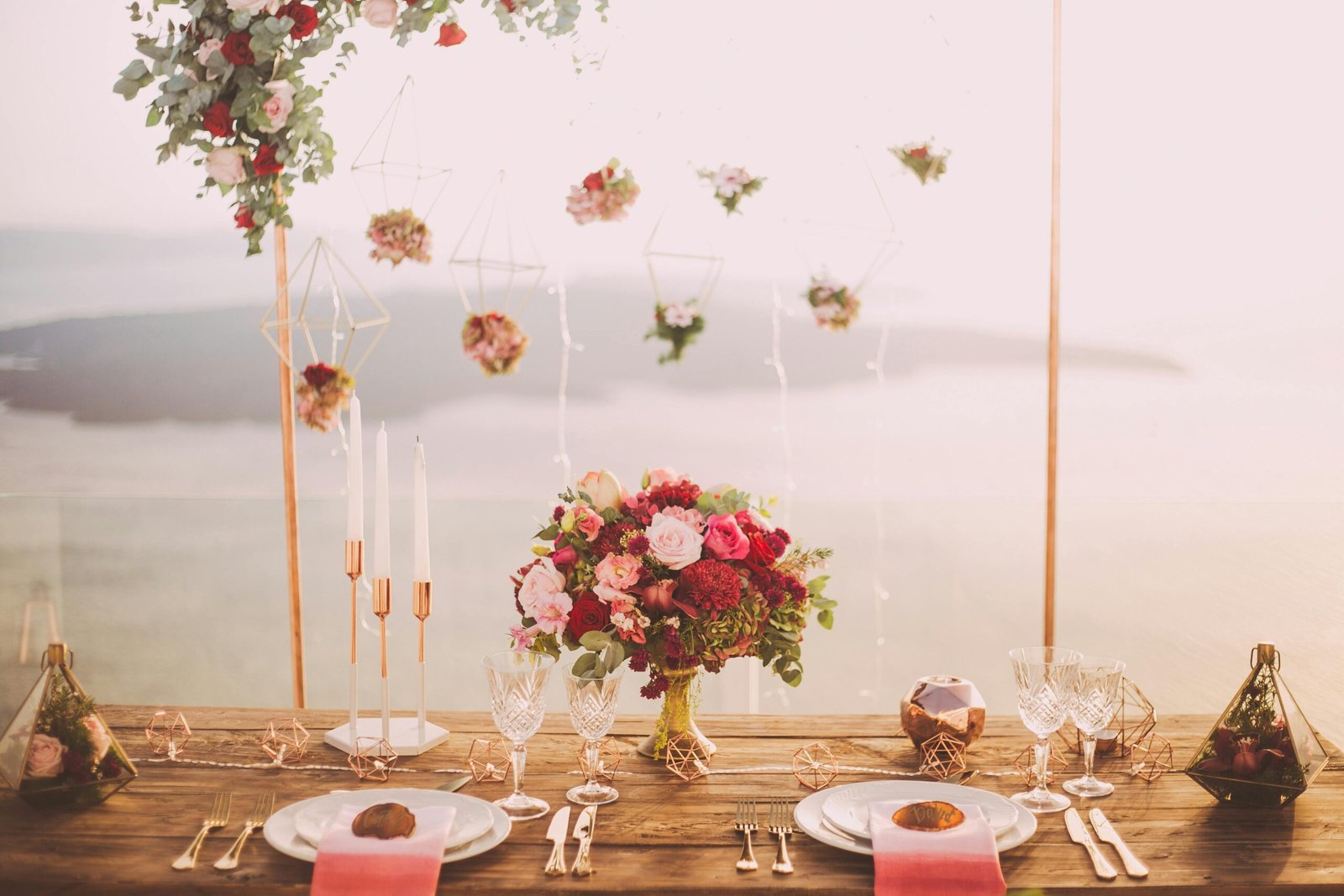 Romantic dining setup with flowers and candles overlooking Santorini waterscape at sunset.