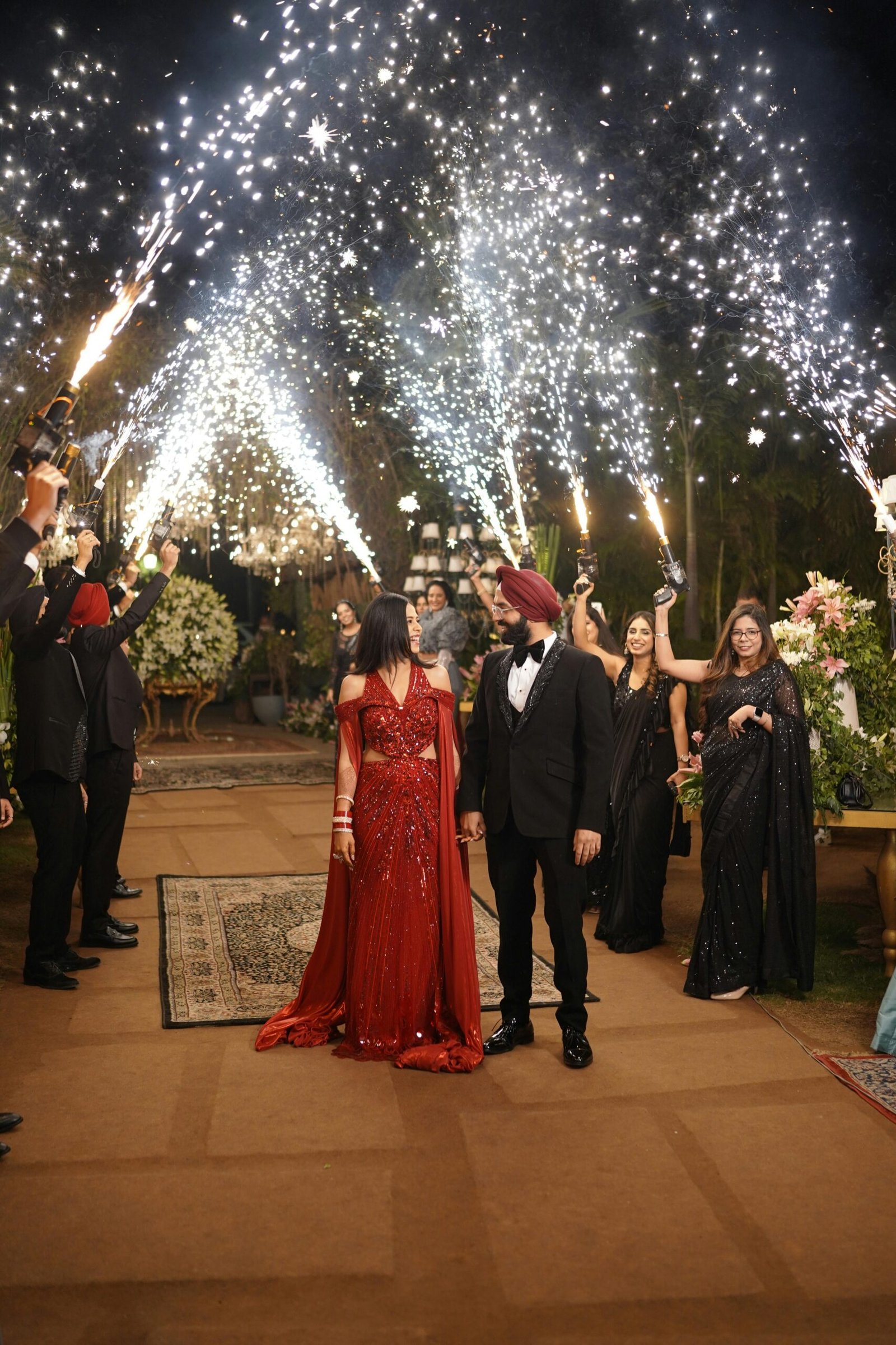 Elegant couple in formal attire celebrating under sparklers during a nighttime party in Chandigarh, India.